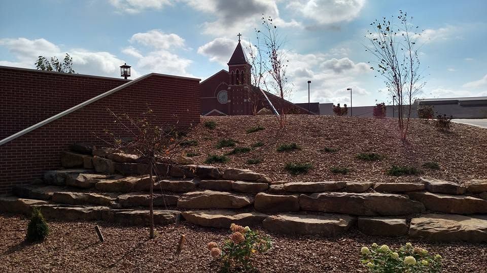 Multi-tiered natural stone retaining wall on a mulched hillside with a church steeple in the background
