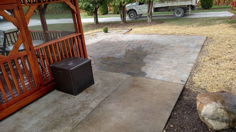 Stone retaining wall with tree and plantings beside a gray residential home