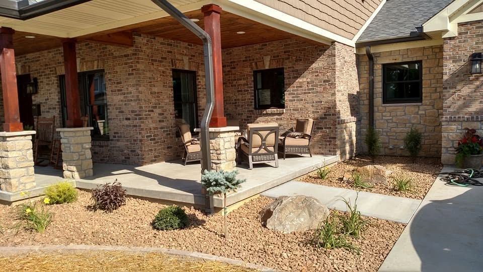 Covered brick patio with outdoor seating, stone pillars, and a gravel landscape bed featuring a large boulder