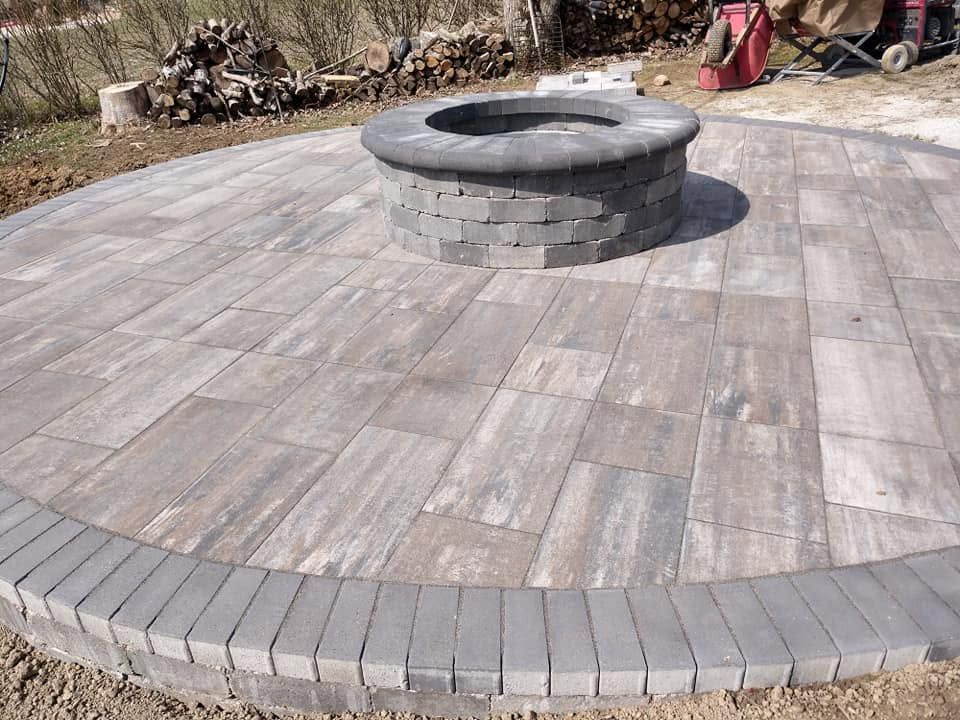 Circular gray stone block fire pit centered on a newly installed paver patio with a neat stone border
