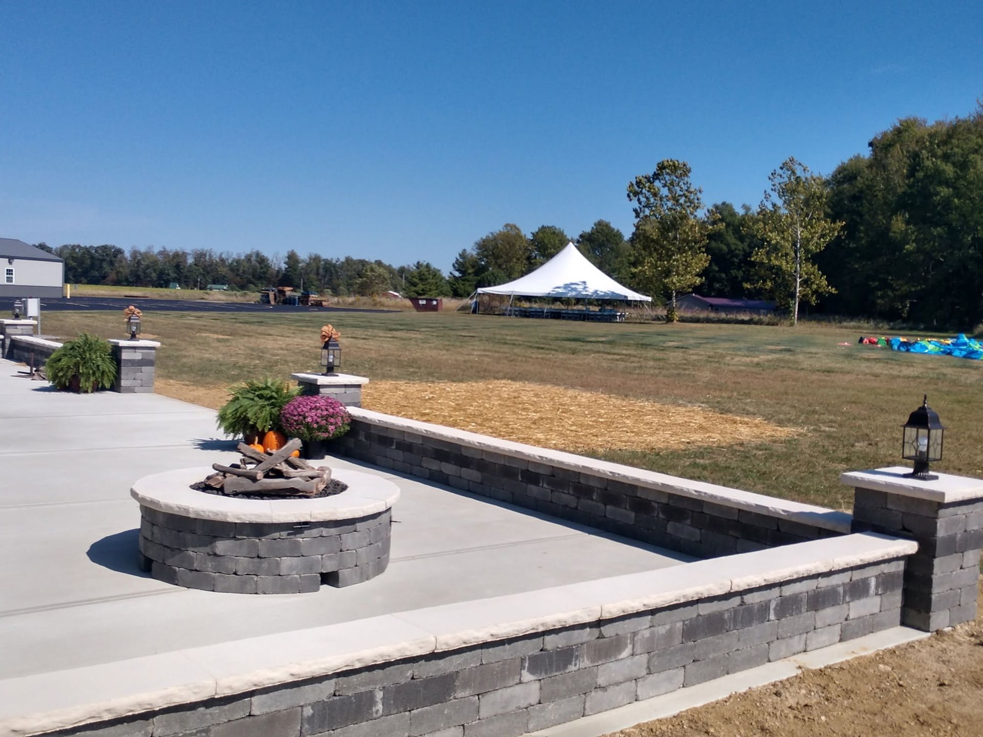 Stone block fire pit and curved seating wall on a concrete patio overlooking a wide open field with a white event tenT