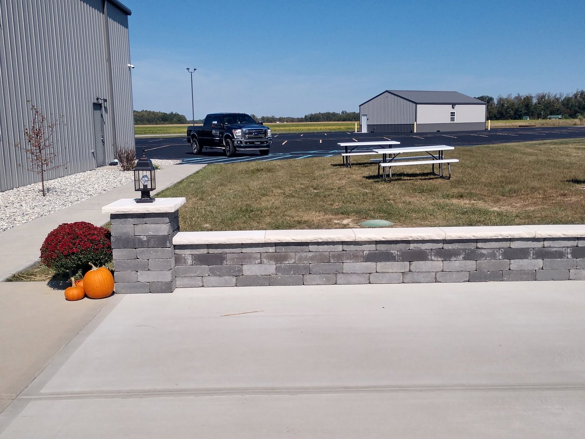 Low stone wall and column light looking out toward a grassy lawn with picnic tables and a commercial property