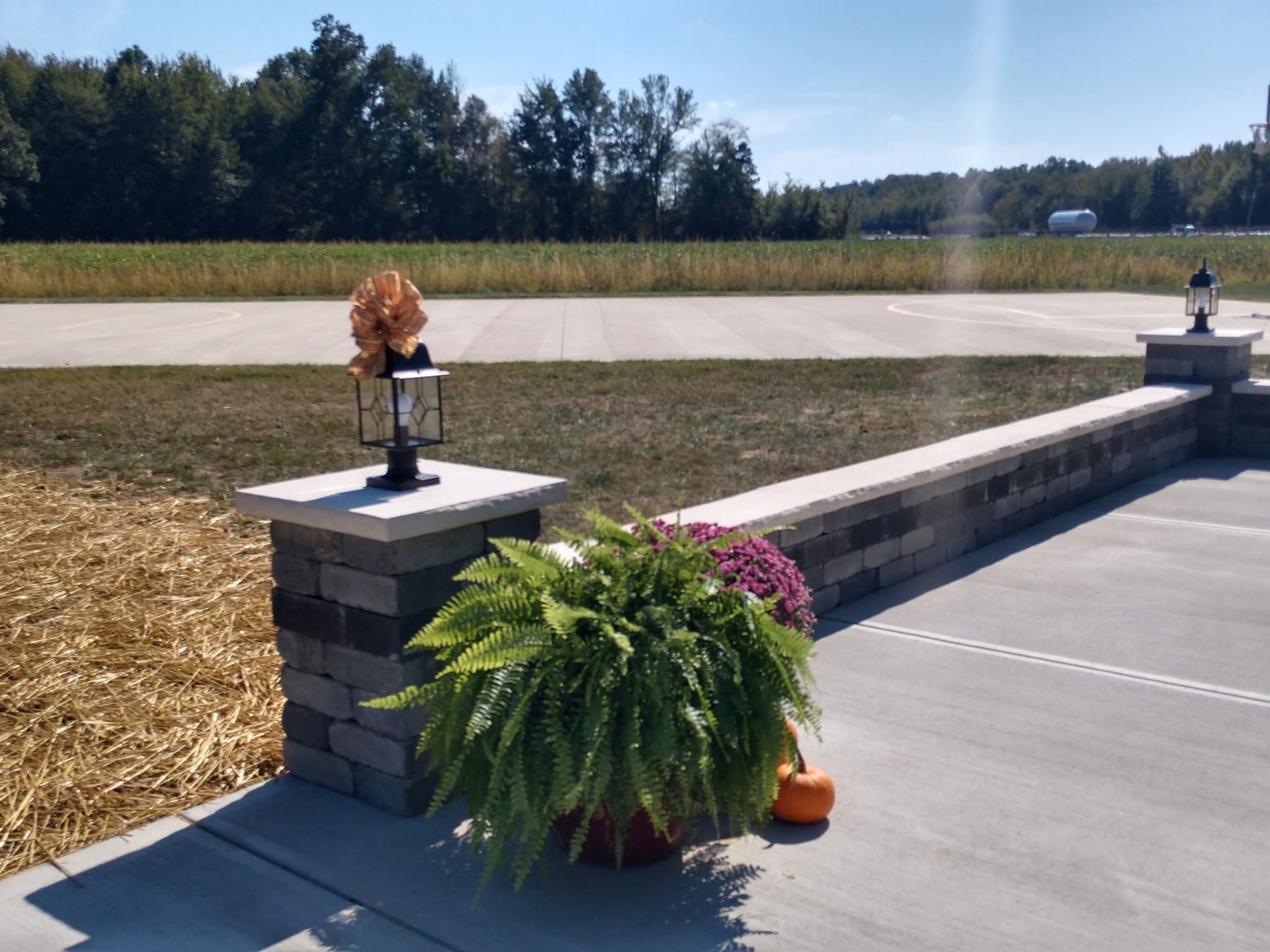 Stone masonry pillar with an outdoor lantern light fixture next to a walkway decorated with potted ferns and autumn accents