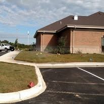Corner view of a brick commercial building with stone accents, a concrete curb, and an asphalt parking lot