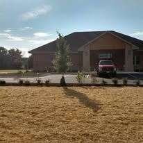 Newly seeded and strawed lawn area with a young tree in front of a brick commercial facility