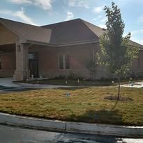 Main entryway of a newly constructed brick building with fresh grading, straw, and young ornamental trees
