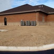 Exterior utility area of a brick building with commercial HVAC units and newly leveled soil ready for landscaping