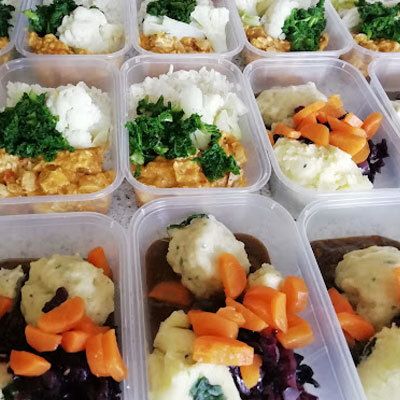 Meal prep containers with rice, greens, roasted carrots, and mashed potatoes arranged in rows