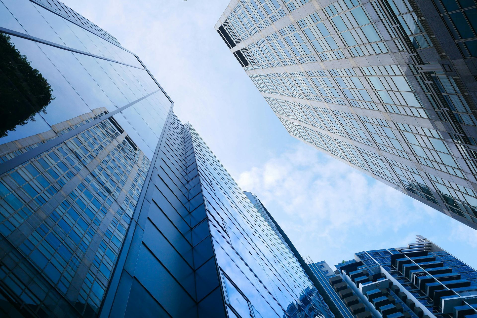 Skyscrapers reaching towards a partly cloudy sky. Reflective glass facades, blue hues.