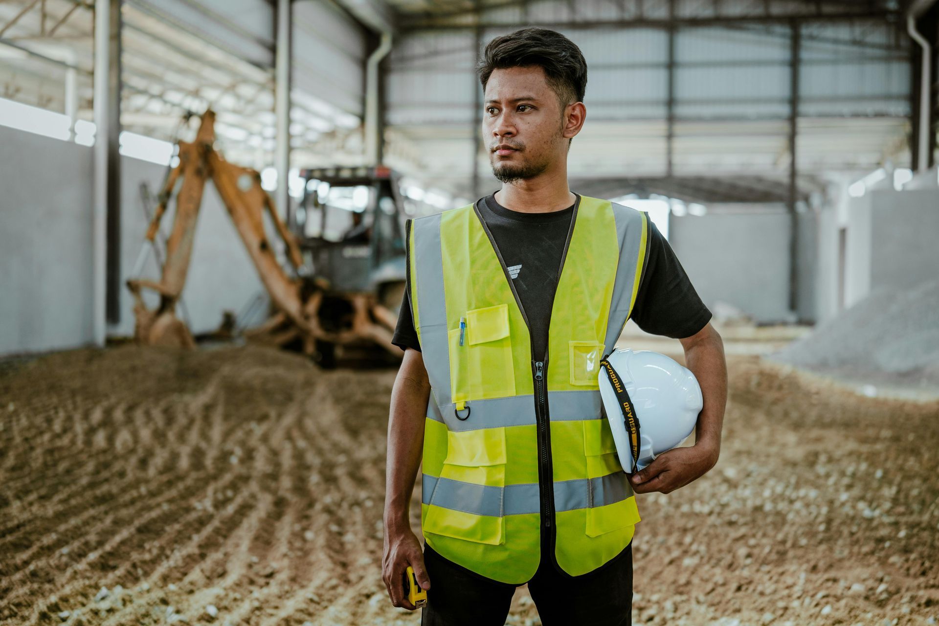 Construction worker in yellow safety vest holding hard hat in warehouse, representing Forte Safe safety consulting services