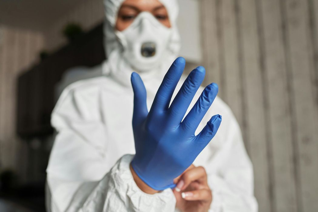 Person in hazmat suit putting on blue gloves, representing Forte Safe safety, contamination control, and protective services