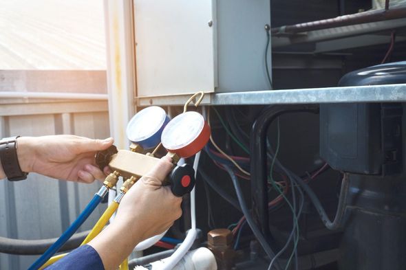 Person connecting gauges to an air conditioning unit; red and blue gauges.
