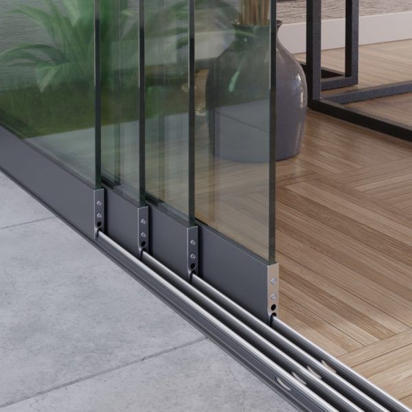 Detailopname van een modern schuifdeursysteem van glas met grijze metalen frames en rails, waarbij de vloerrail in beeld is.