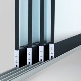 Een close-up van een meerdelig schuifdeursysteem van glas, met de verticale frames, metalen wielen en vloerrails.