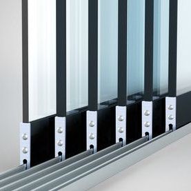 Een close-up van een meerdelig schuifdeursysteem van glas met verticale zwarte frames gemonteerd op zilverkleurige vloerrails.