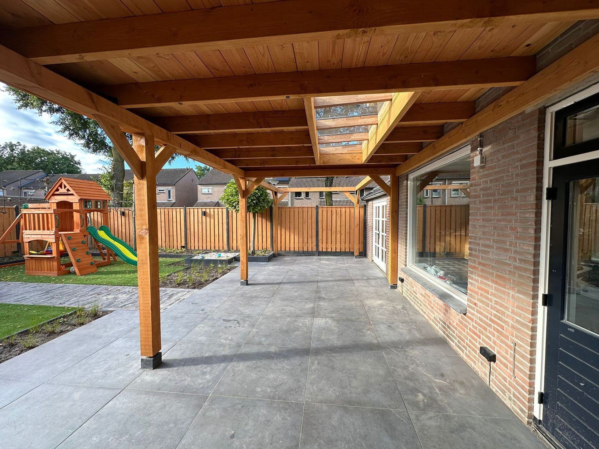 Een bakstenen huis met een houten veranda en een speeltuin in de achtertuin.