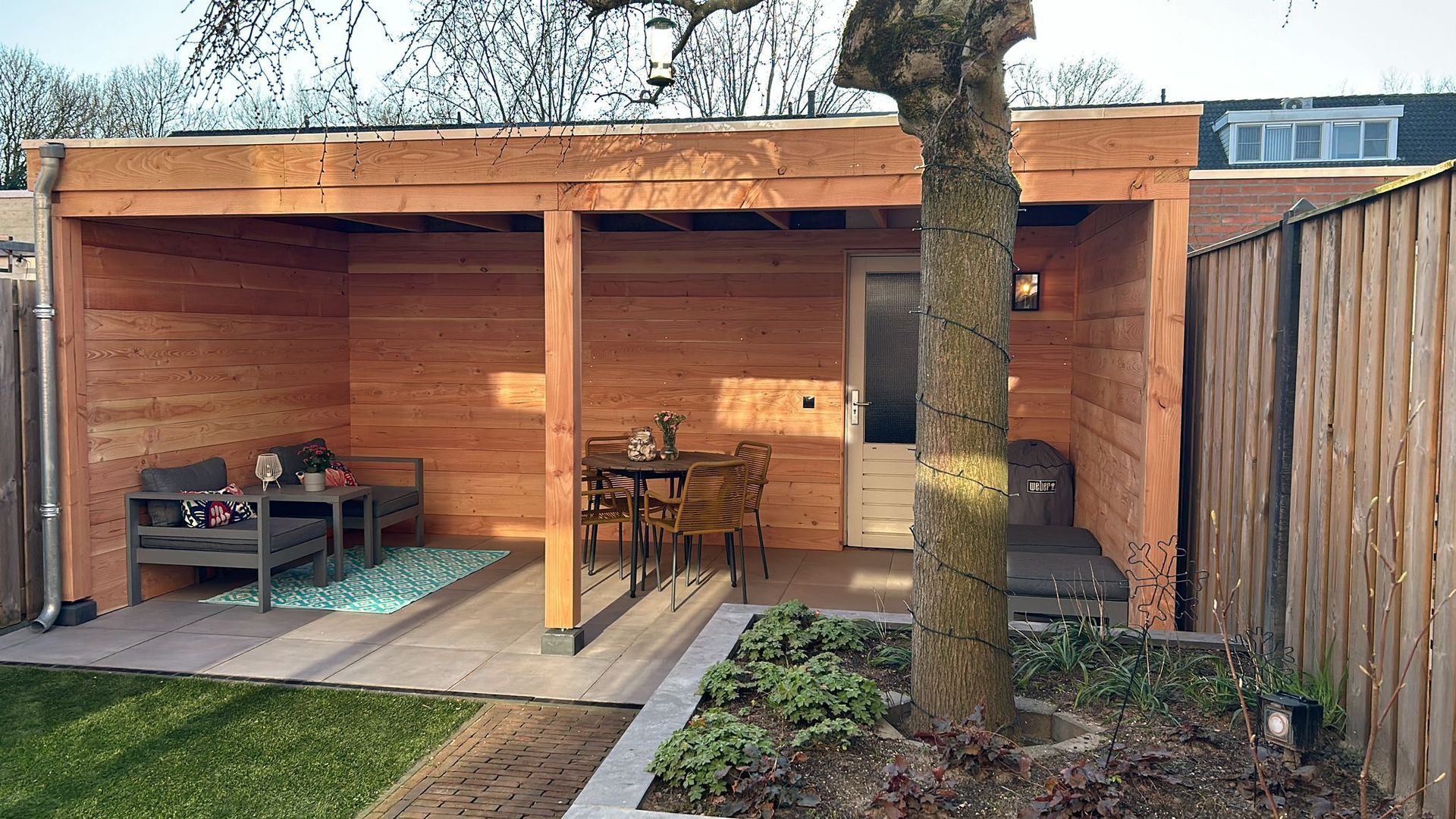 Een houten schuilplaats met een tafel en stoelen in een achtertuin.