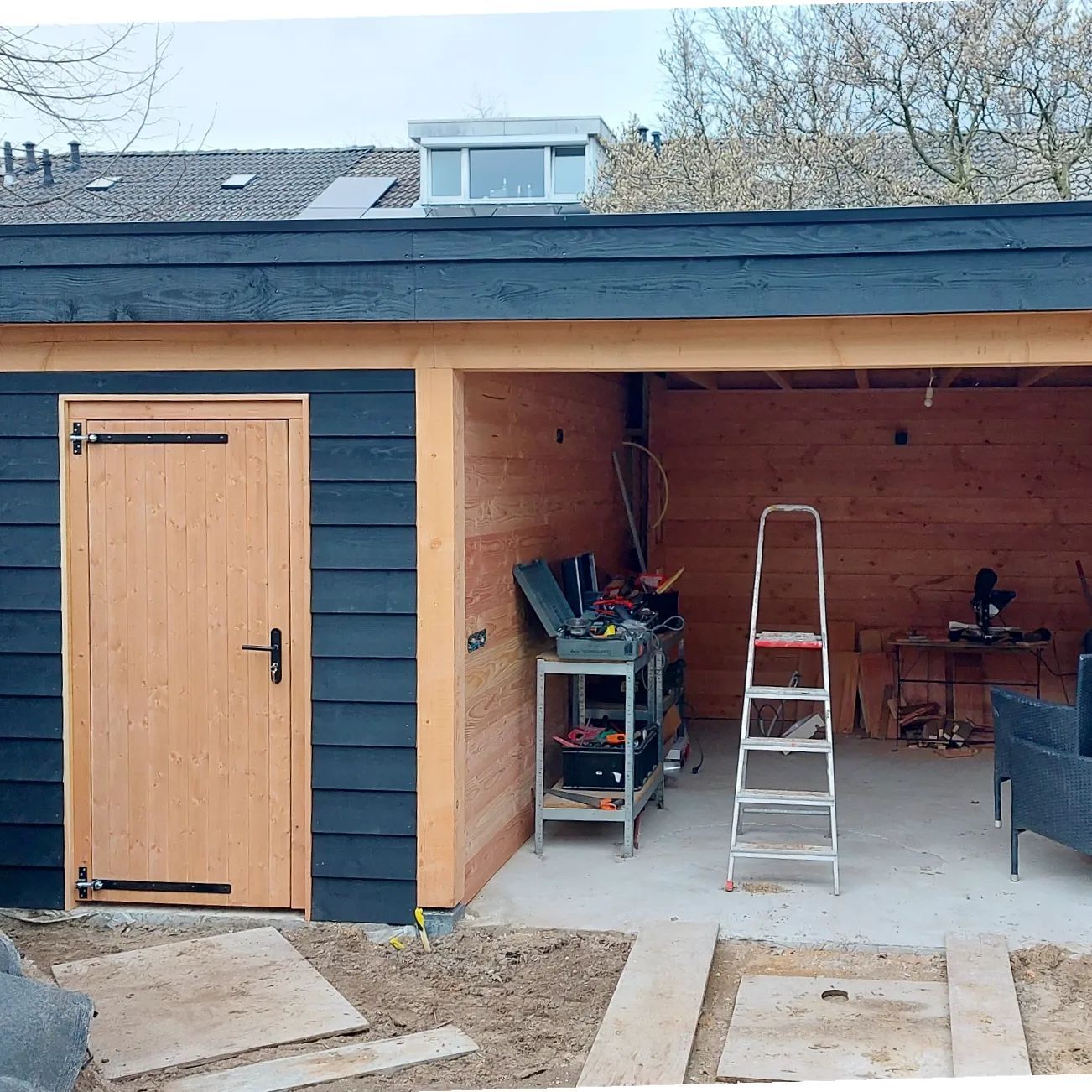 Een houten schuur met een zwart dak en een houten deur