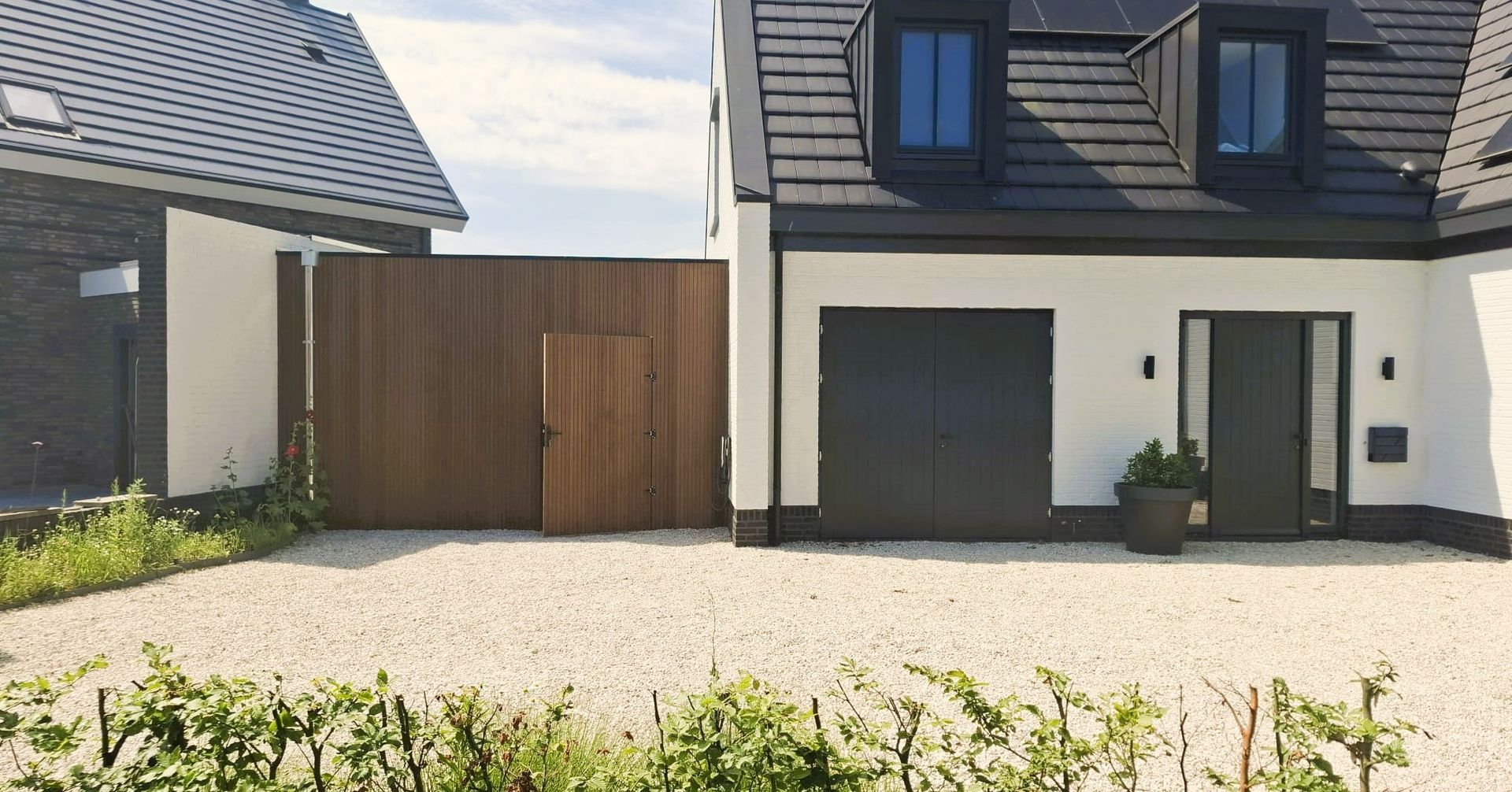 Een wit huis met een zwarte garagedeur en een houten poort