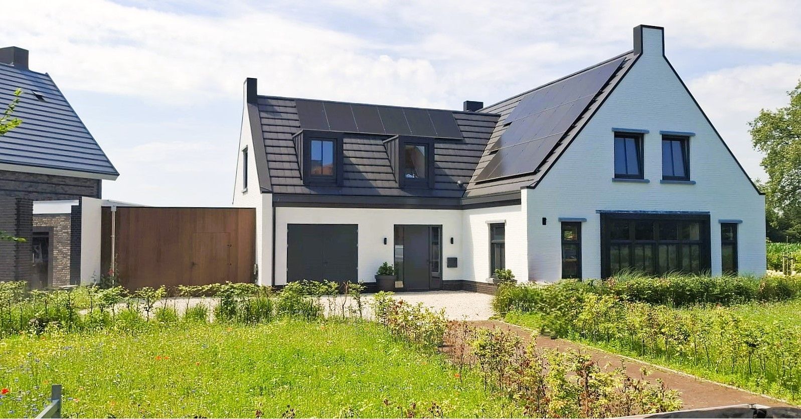 Een wit huis met een zwart dak staat naast een bakstenen huis.