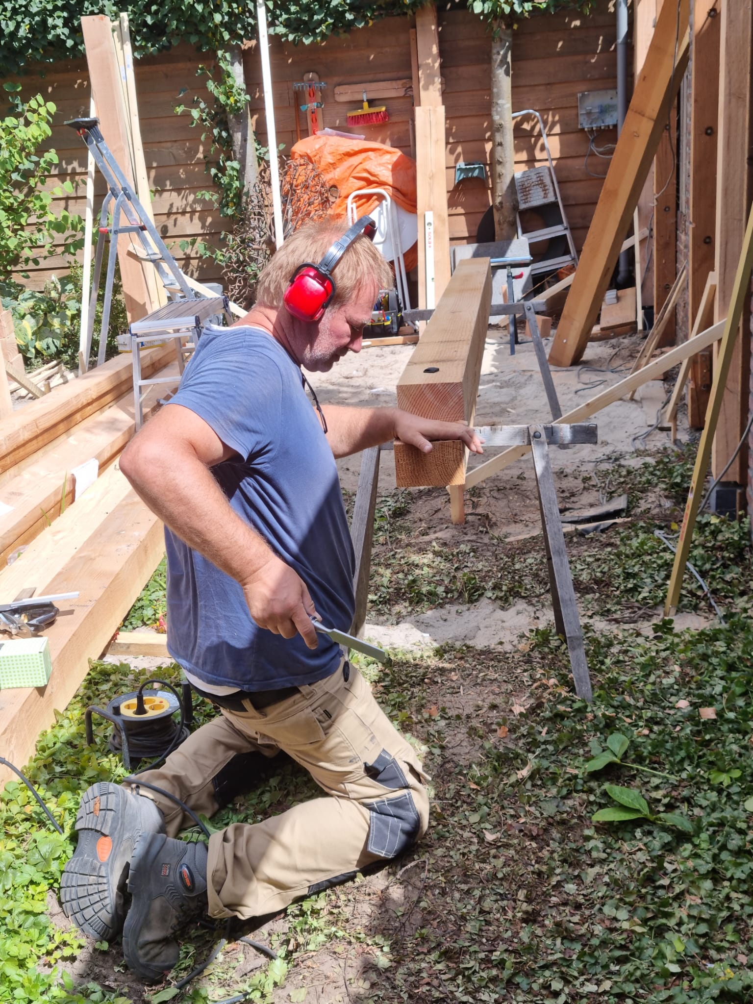 Een man met oorkappen knielt voor een stapel hout.