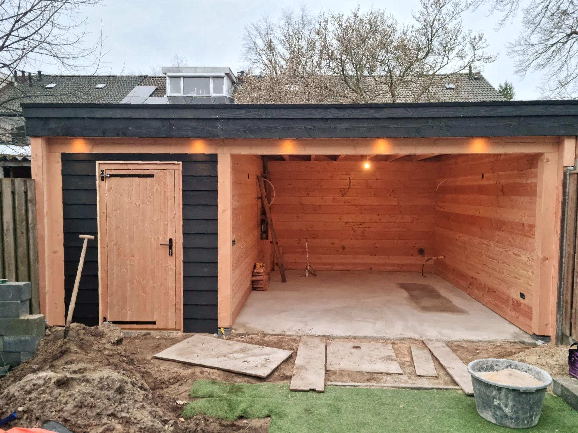 Er wordt een houten garage gebouwd in de achtertuin van een huis.
