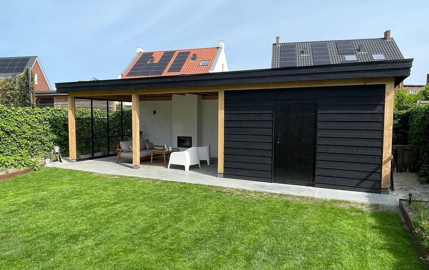 Een zwarte schuur met een overdekt terras in de achtertuin van een huis.