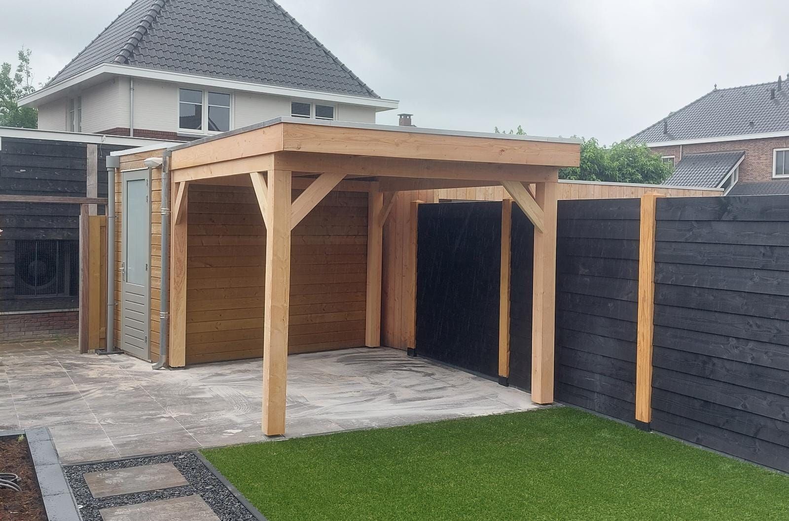 Een achtertuin met een houten constructie en een zwart hek