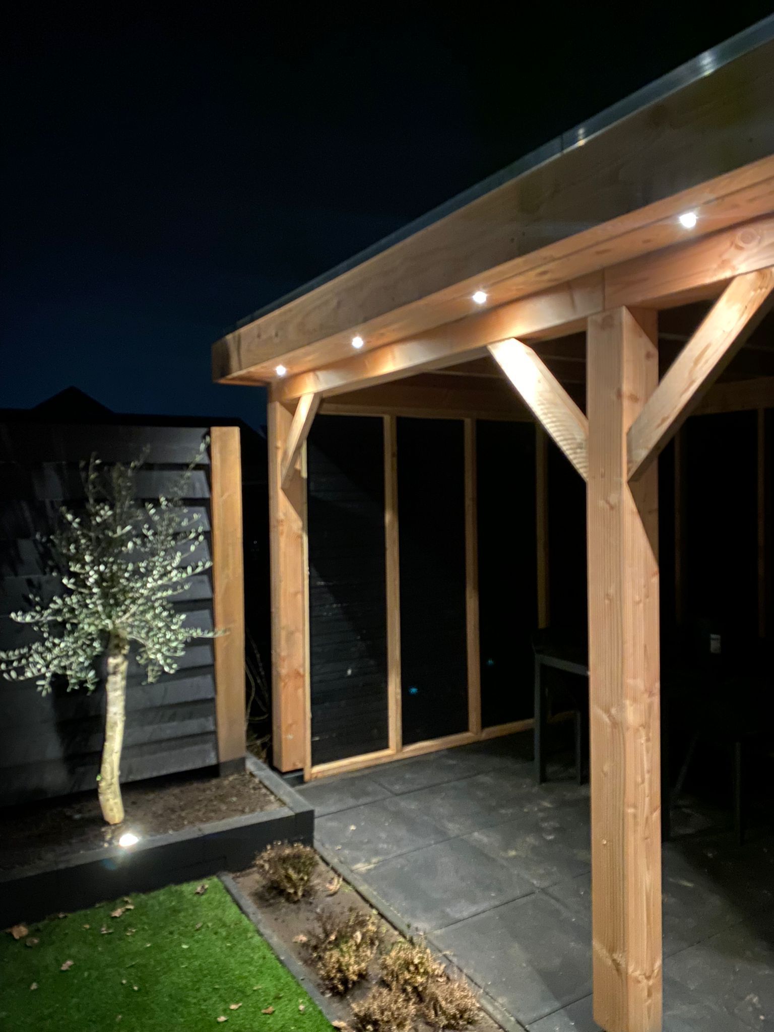's Avonds wordt een houten pergola in de achtertuin verlicht.