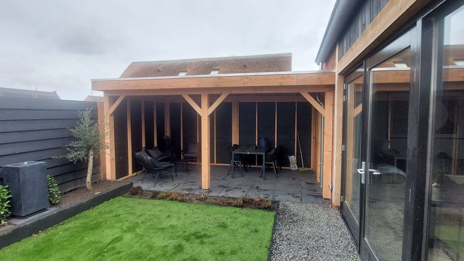 Een houten pergola staat in de achtertuin van een huis.