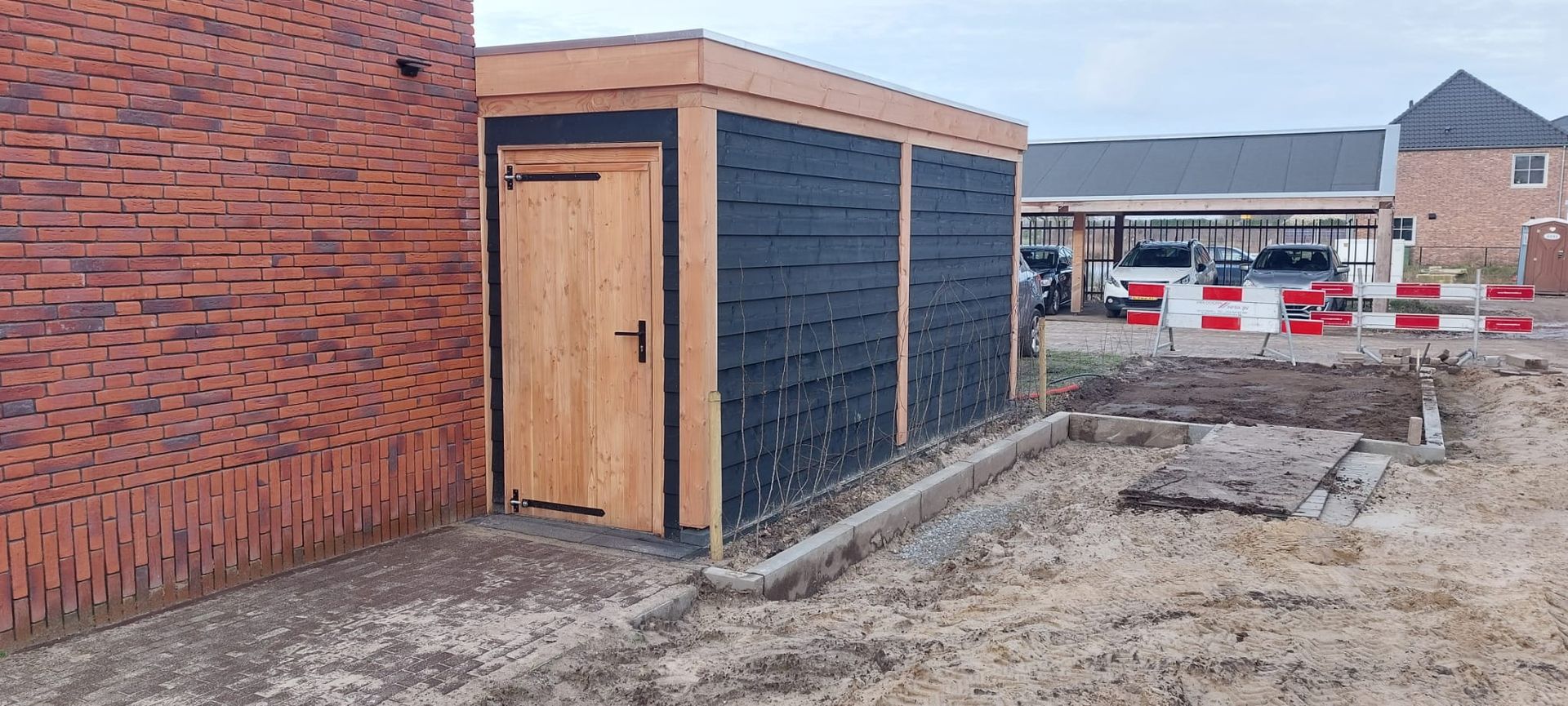 Een houten schuur staat naast een bakstenen gebouw.