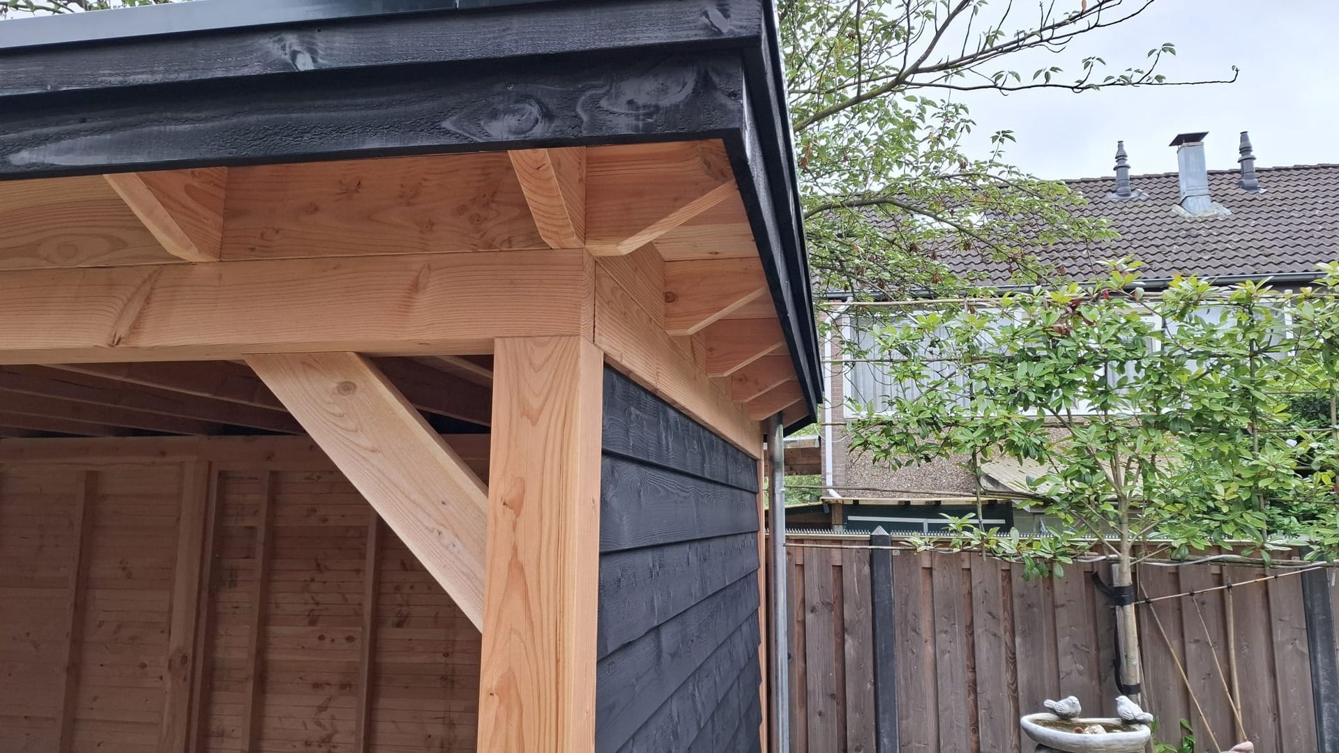 Een houten schuur met een zwart dak staat naast een houten hek.