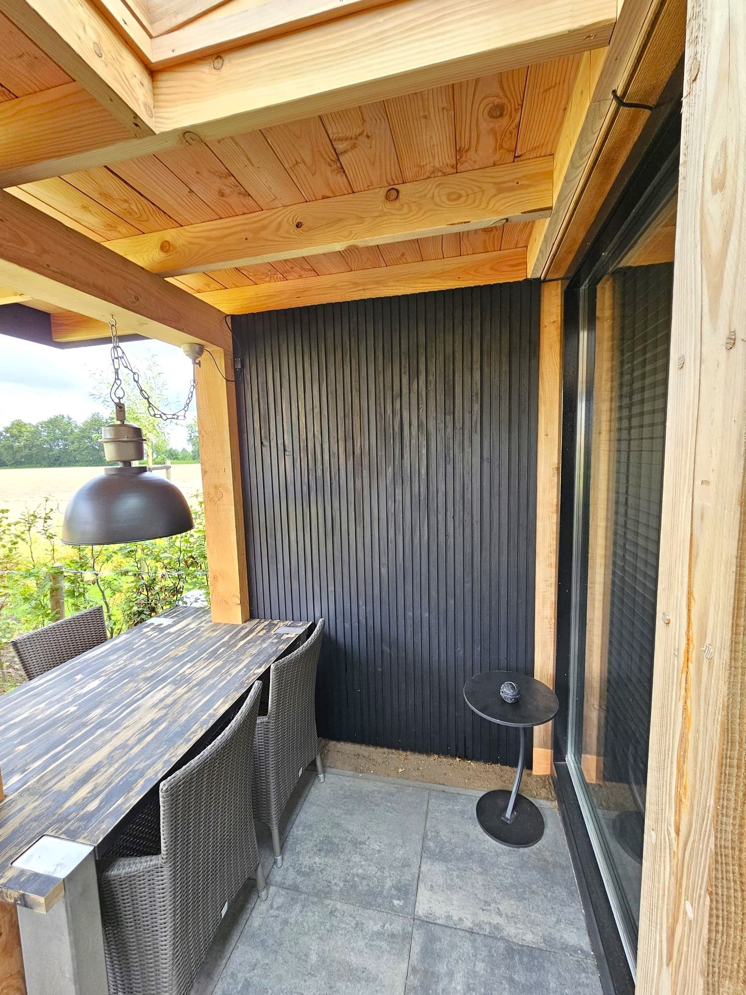 Een terras met een tafel en stoelen onder een houten dak.