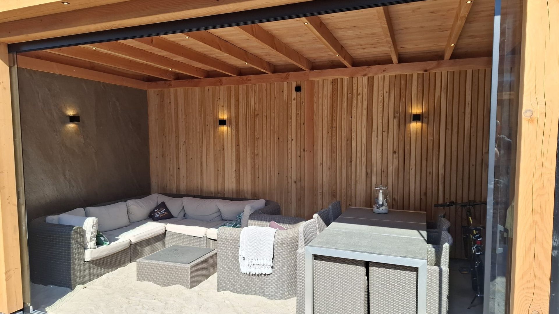 Een woonkamer met een bank, tafel en stoelen onder een houten dak.
