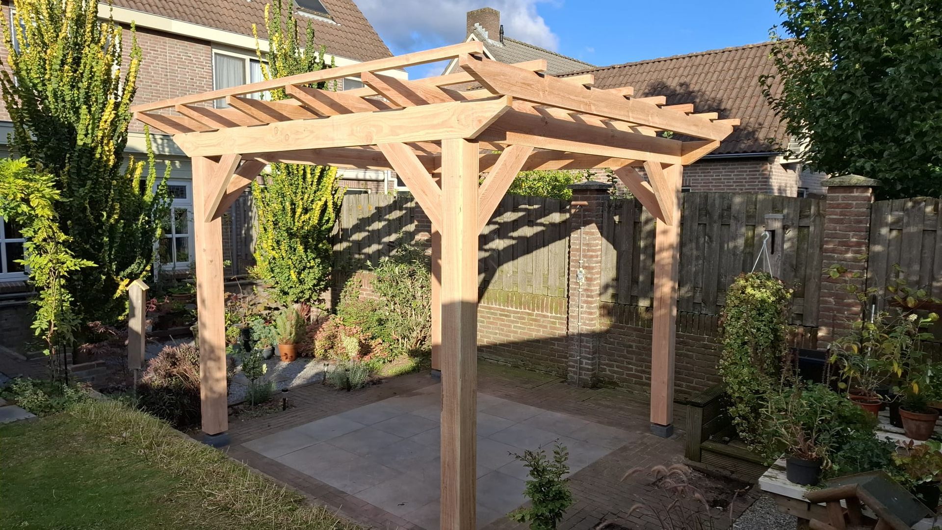 In een achtertuin staat een nieuw gebouwde houten pergola boven een betegeld terras.