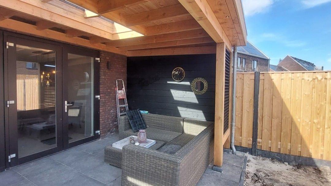 Een terras met een bank en een tafel onder een houten dak.