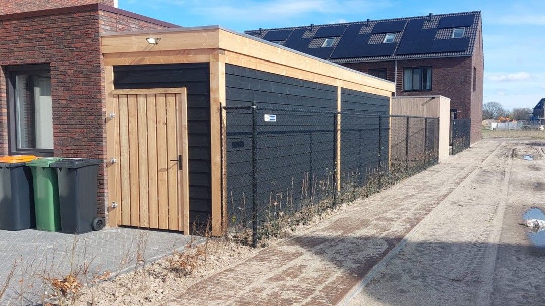 Een houten schuur staat naast een bakstenen gebouw.