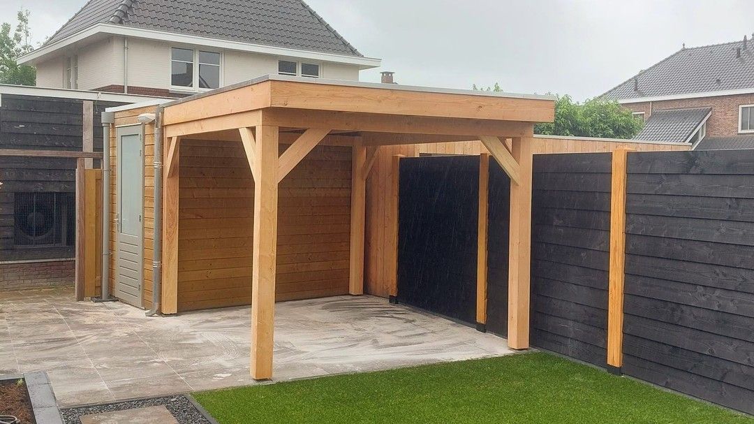 Een houten pergola staat midden in de achtertuin, naast een hek.