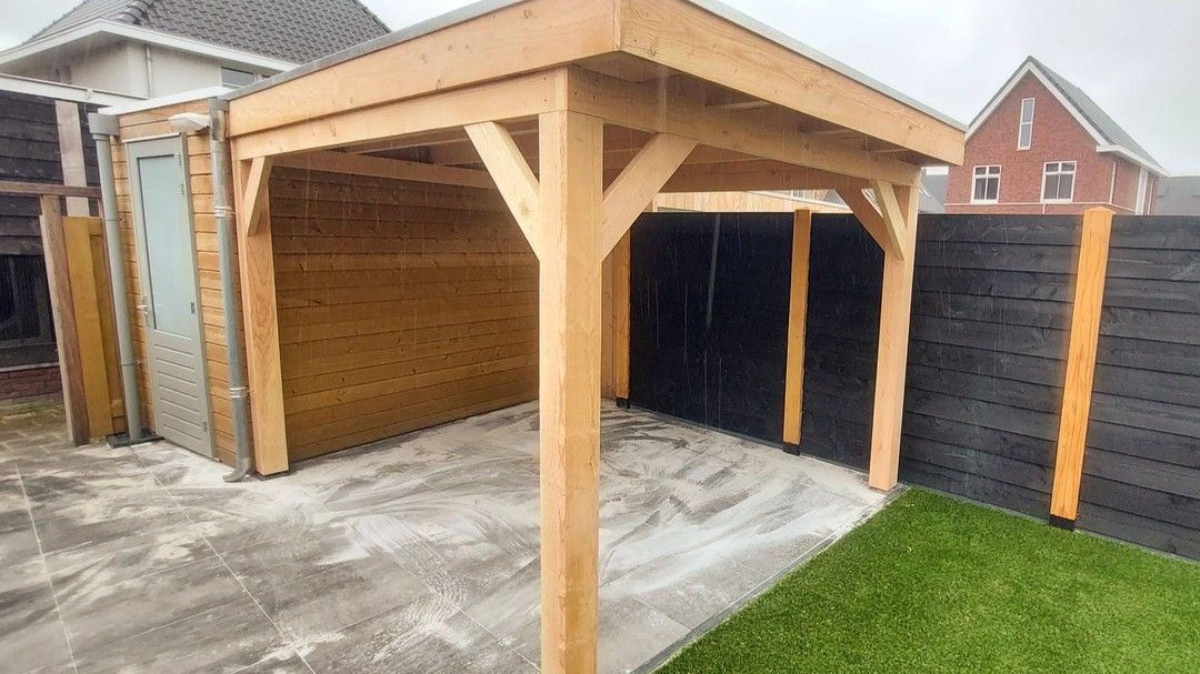 Een houten schuur staat in een achtertuin naast een hek.