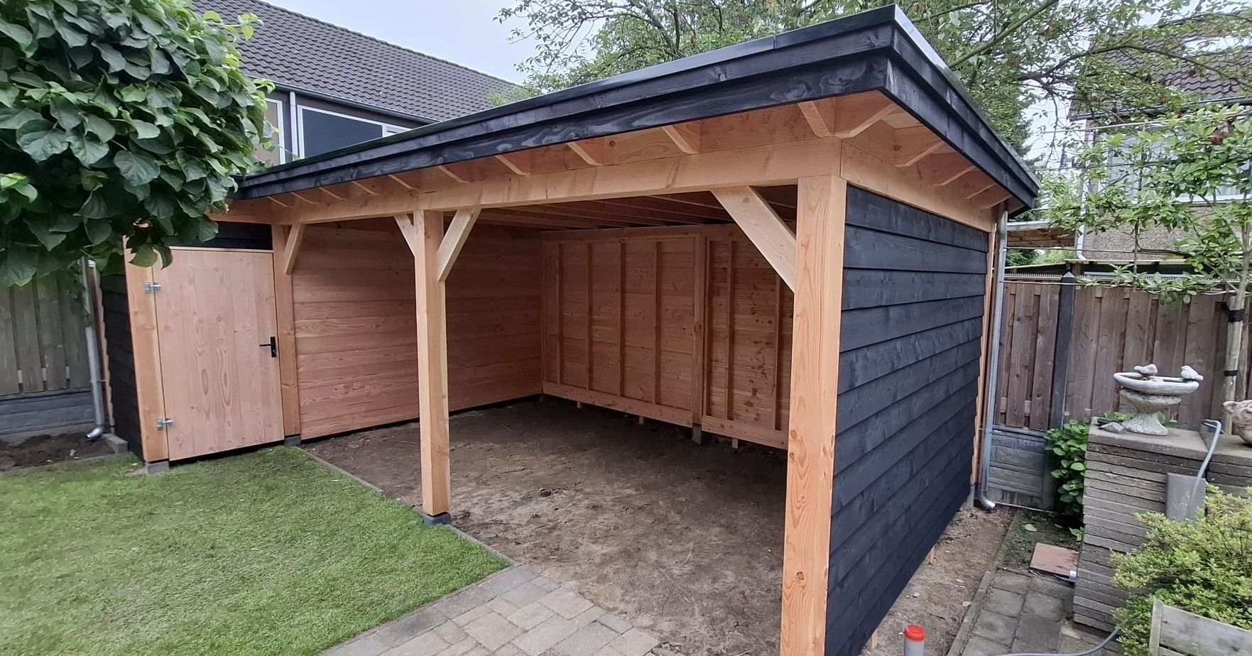 Een houten schuur staat midden in een achtertuin.