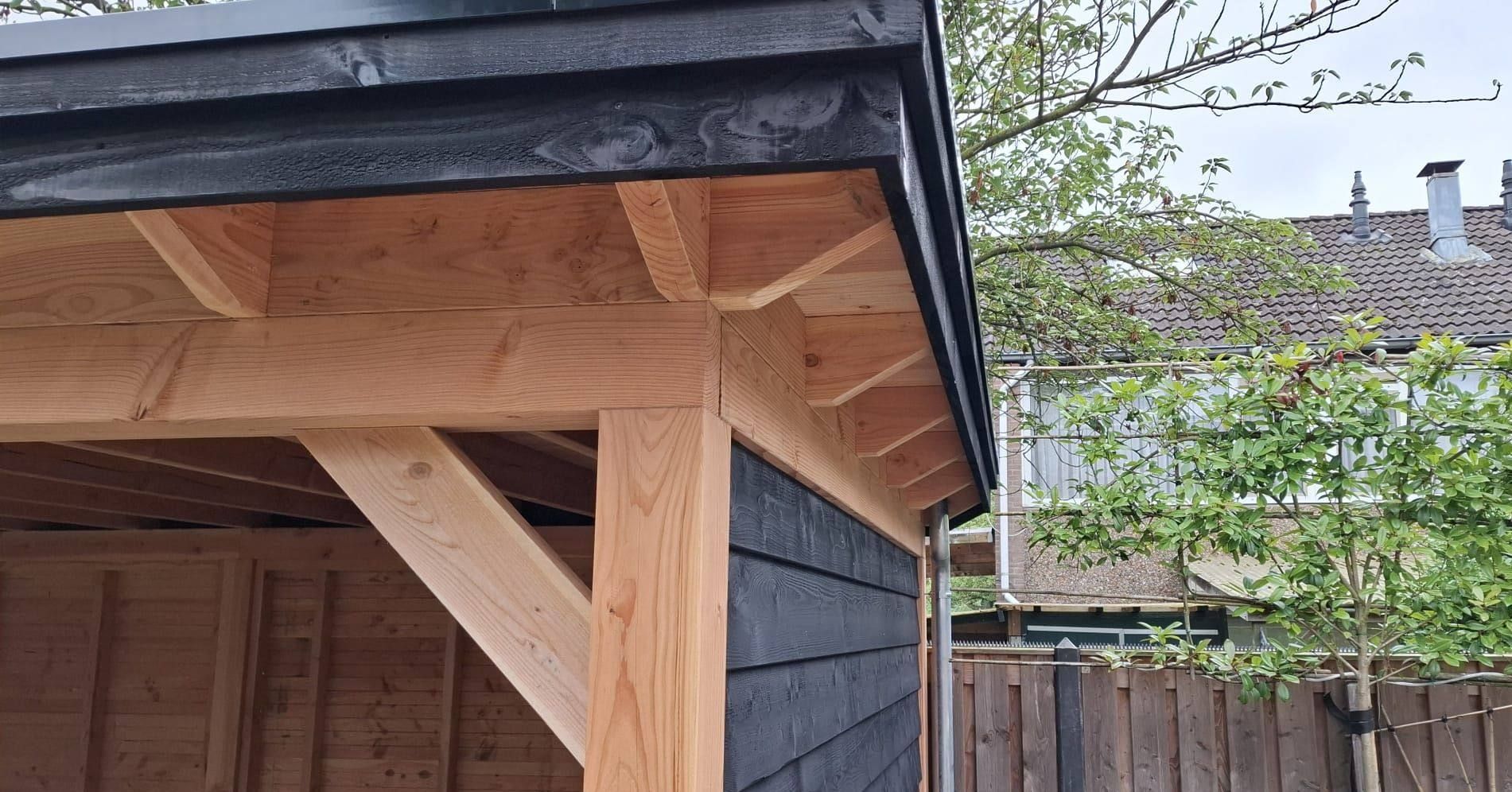 Een houten constructie met een zwart dak en een houten hek op de achtergrond.