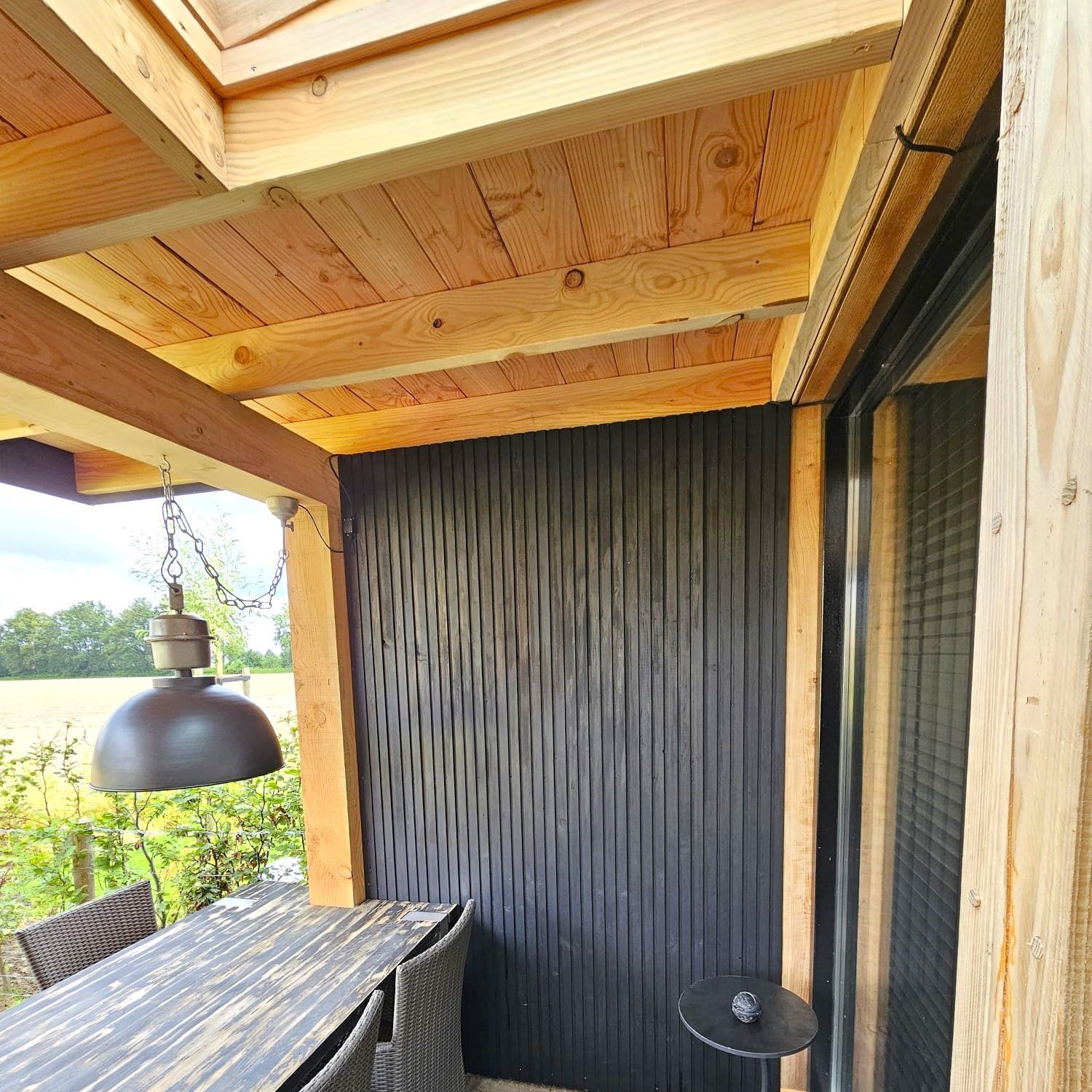 Een terras met een tafel en stoelen onder een houten dak