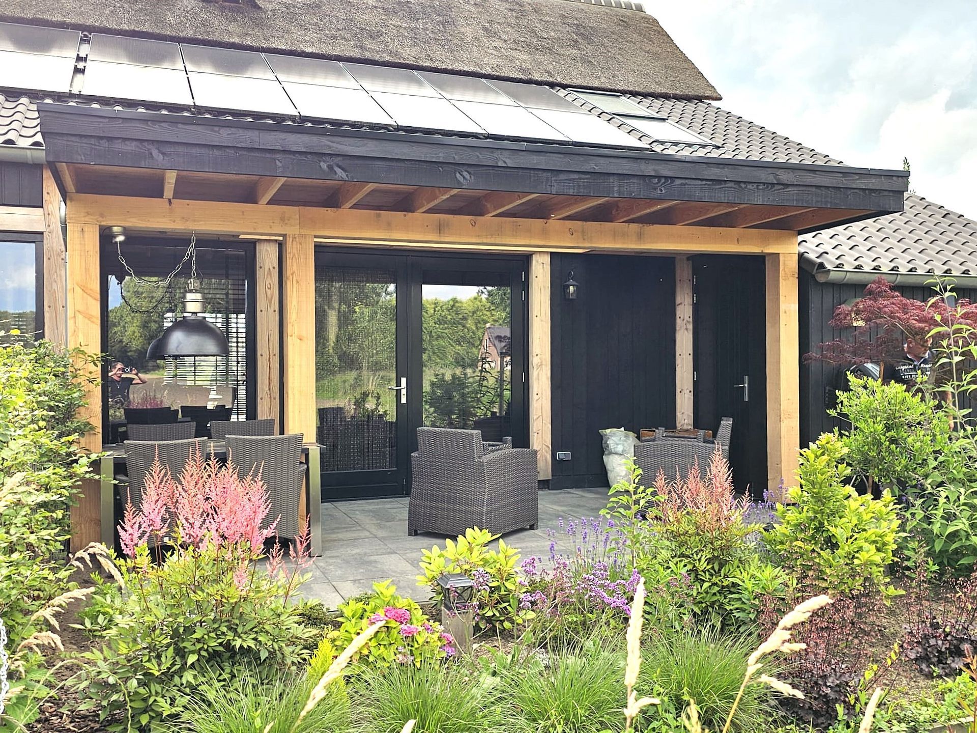 Een huis met een rieten dak en een terras met stoelen en tafels.