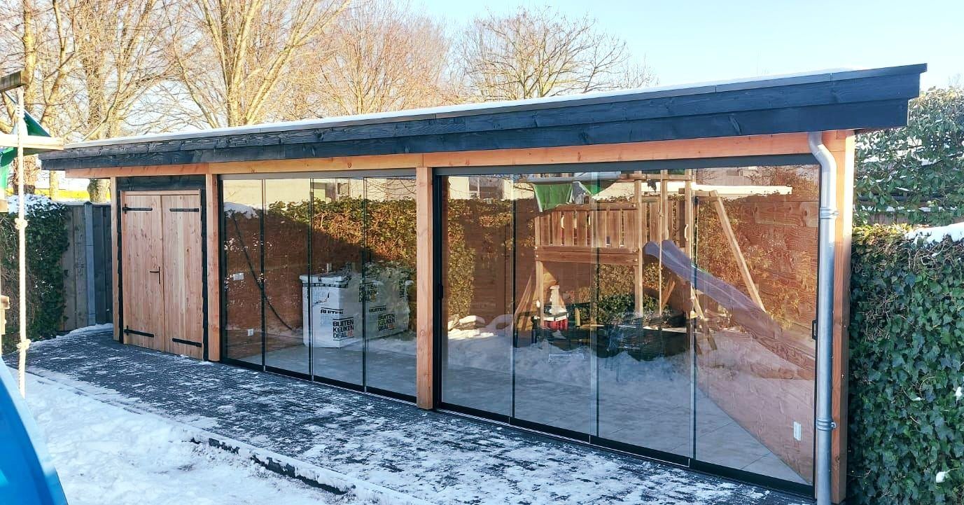 Een groot houten gebouw met glazen schuifdeuren is bedekt met sneeuw.