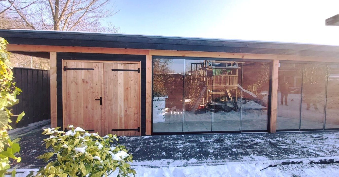 Een houten garage met glazen schuifdeuren en een speeltuin op de achtergrond.
