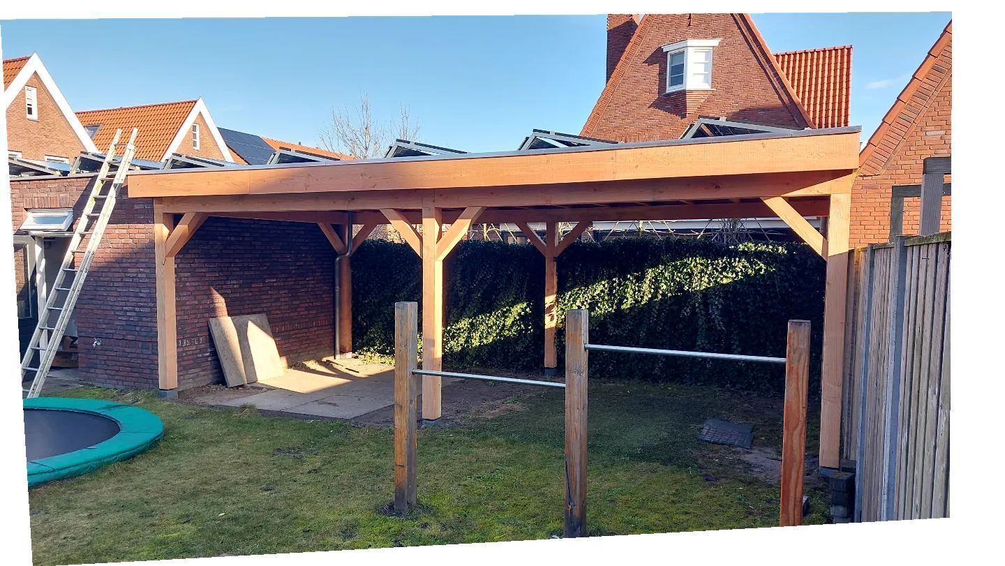 In de achtertuin, naast een trampoline, wordt een houten constructie gebouwd.