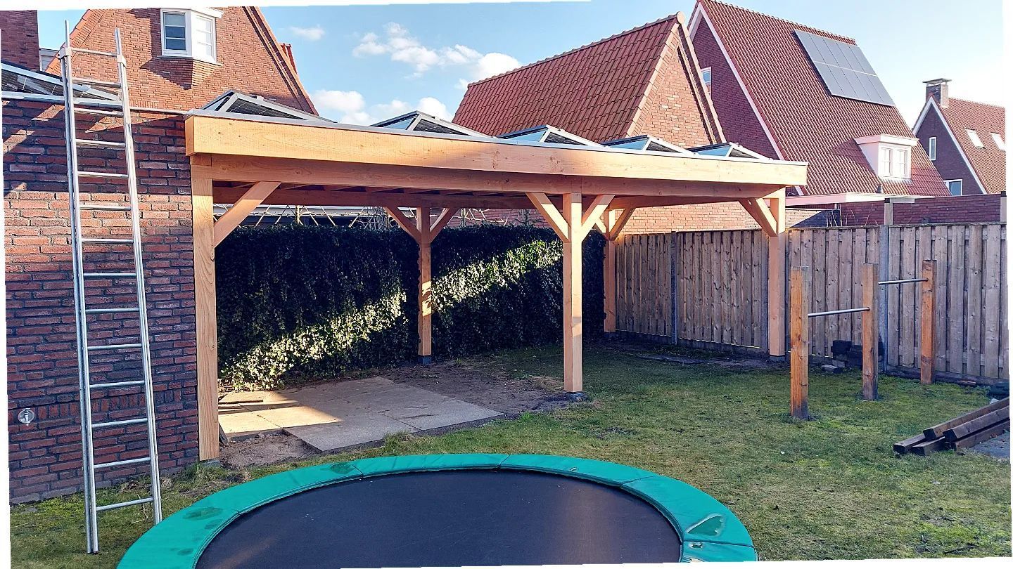 In de achtertuin, naast een trampoline, wordt een houten carport gebouwd.