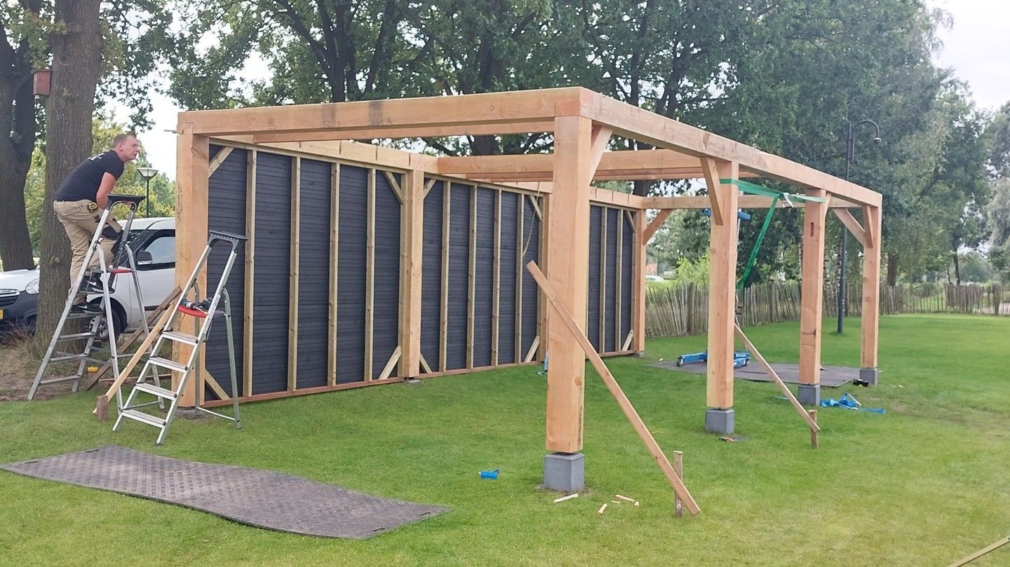 Een man staat op een ladder naast een houten constructie.