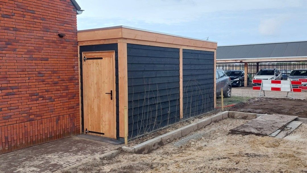 Een houten schuur staat naast een bakstenen gebouw.