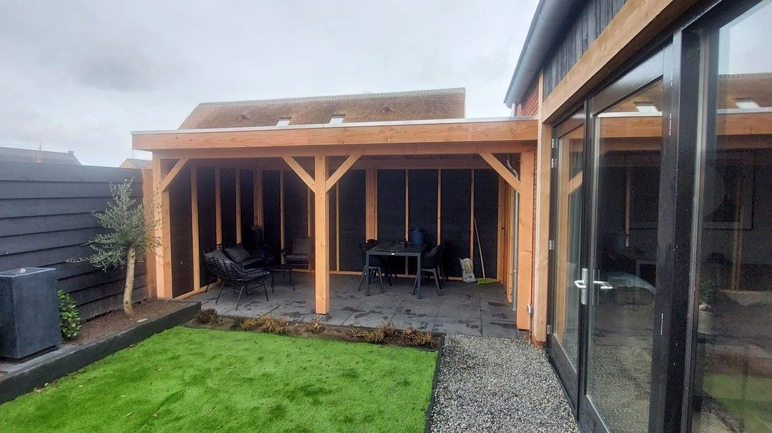 Een houten prieel in de achtertuin van een huis met glazen schuifdeuren.